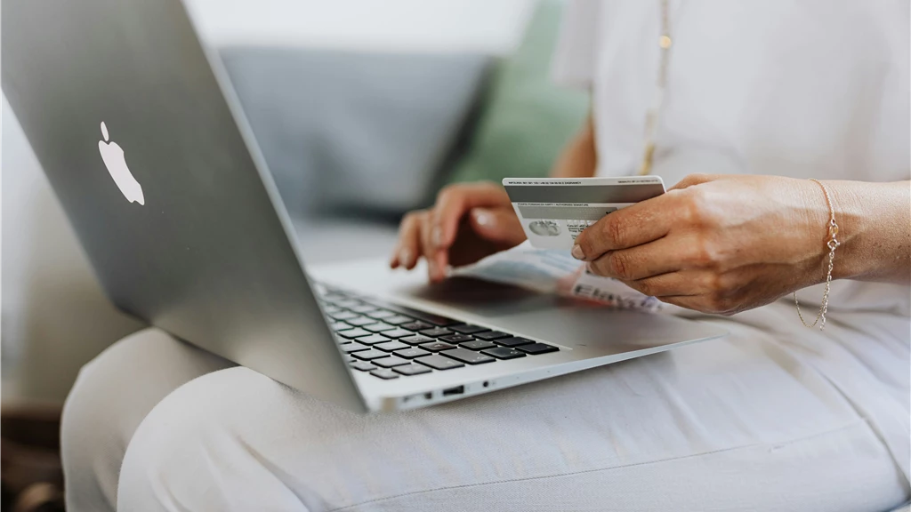 Person Using a Macbook and Holding a Credit Card